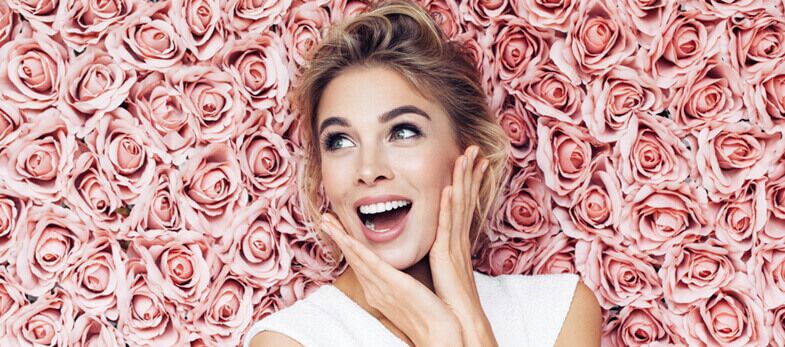 Composite Bonding Wimbledon - A radiant woman with a joyful expression lies amidst a backdrop of lush pink roses, her hands gently touching her cheeks, showcasing a bright, well-cared-for smile possibly enhanced by composite bonding treatments from Ridgway Dental, a dental clinic in Wimbledon. Her sparkling eyes and open, vibrant smile illustrate the confidence and satisfaction that come with quality dental care. This image not only highlights the beauty and natural appearance of composite dental bonding but also reflects the aesthetic focus and patient-centered care at Ridgway Dental, where such cosmetic procedures help perfect and brighten smiles.
